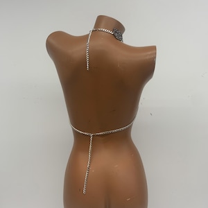 May include: Silver chain body jewelry with a choker necklace. The chain is connected to a small piece of fabric at the back.