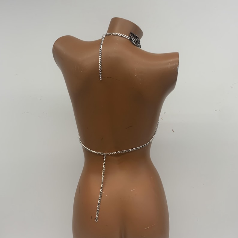 May include: Silver chain body jewelry with a choker necklace. The chain is connected to a small piece of fabric at the back.
