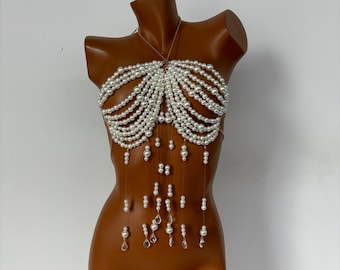 Op de afbeelding: Een witte parel- en kristallen body chain met een delicaat ontwerp. De ketting heeft een gelaagd, cascade-effect met parels en kristallen die van het midden hangen.