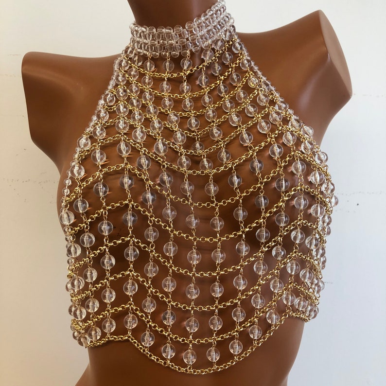May include: A gold chain body jewelry piece with clear plastic beads. The chain is layered and forms a mesh pattern.