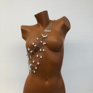 May include: A silver chain body jewellery piece with white pearl accents. The chain is layered and features a teardrop design.