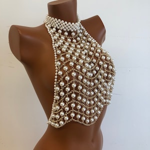 May include: A gold chain body jewelry piece with white pearls. The chain is made of small, linked rings with a pearl attached to each ring.