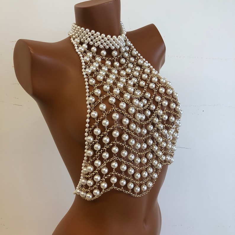 May include: A gold chain body jewelry piece with white pearls. The chain is made of small, linked rings with a pearl attached to each ring.