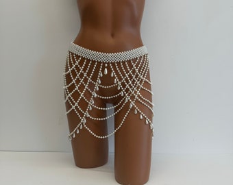 May include: A white pearl body chain with a wide band at the waist and multiple strands of pearls with teardrop-shaped beads hanging down.
