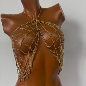 May include: A gold chain body harness with a web-like design. The chain is made of multiple layers and has a dangling fringe.