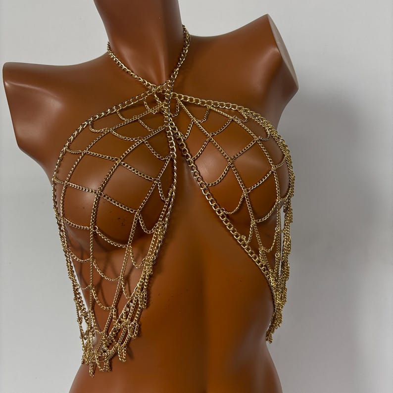 May include: A gold chain body harness with a web-like design. The chain is made of multiple layers and has a dangling fringe.