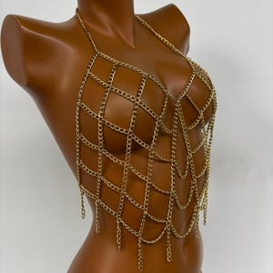 May include: A gold chainmail top with a delicate, intricate design. The top features a web-like pattern with dangling chains.