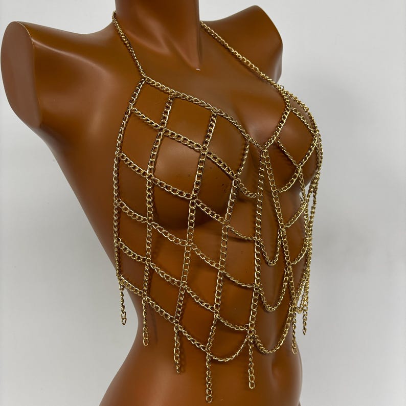 May include: A gold chainmail top with a delicate, intricate design. The top features a web-like pattern with dangling chains.