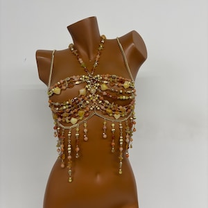 May include: A gold chain body jewelry piece with orange, peach, and yellow beads. The piece has a halter style neckline and a fringe bottom.