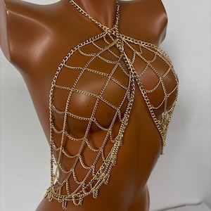 May include: A gold chain body jewelry piece with a web-like design. The chain is made of multiple layers of small linked chains.