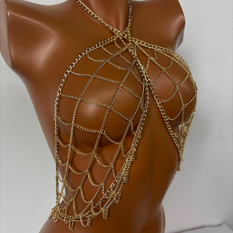 May include: A gold chain body jewelry piece with a web-like design. The chain is made of multiple layers of small linked chains.