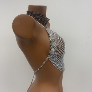 May include: Silver chainmail halter top with a black rhinestone choker. The top is made of multiple layers of chain links and has a long chain that hangs down the back.