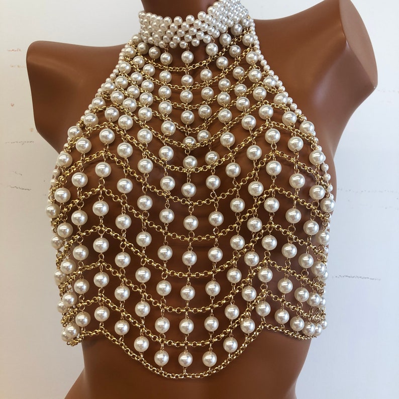 May include: A gold chain body jewelry piece with white pearls. The chain is made of small, linked rings and the pearls are evenly spaced throughout the piece.