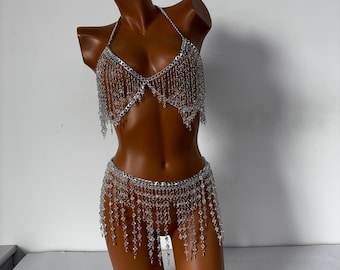 May include: A silver body chain with crystal beads and fringe. The chain is worn as a bra and a skirt.