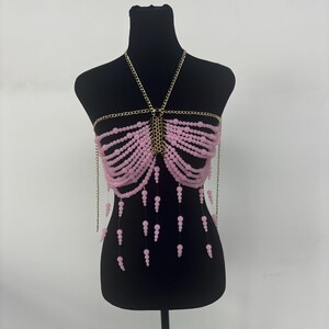 May include: A pink beaded body chain with gold chain accents. The chain is made of small pink beads and has a delicate, feminine look.