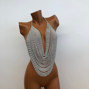 May include: A silver chain body jewelry piece with a V-neck design. The chain is made of many small, linked pieces that create a cascading effect.