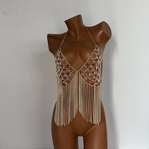 Puede incluir: Una pieza de joyería corporal de cadena dorada con cuentas de cristal transparente y flecos. La cadena está diseñada para ser usada como top.