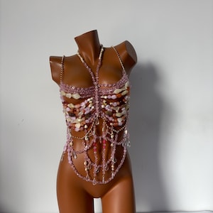 May include: A pink and white beaded top with a layered design. The top is made of various sizes and shapes of beads, including some that are clear and some that are iridescent.