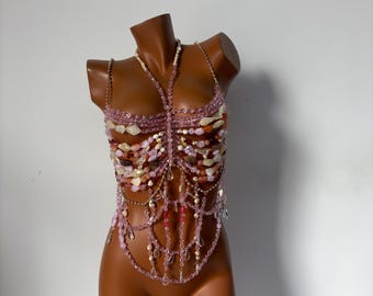 May include: A pink and white beaded top with a layered design. The top is made of various sizes and shapes of beads, including some that are clear and some that are iridescent.