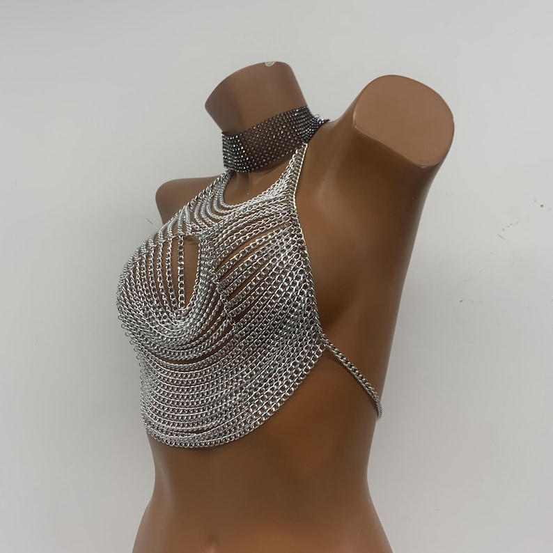 May include: Silver chainmail halter top with a delicate chain detail. The top is made of small, interconnected metal rings, creating a mesh-like appearance.