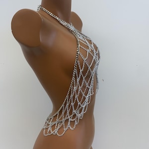 May include: Silver chainmail body jewelry with a halter neck style. The chainmail is made of small, interconnected metal rings.