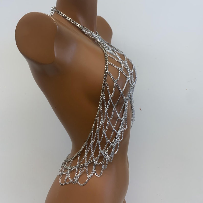 May include: Silver chainmail body jewelry with a halter neck style. The chainmail is made of small, interconnected metal rings.