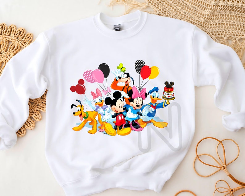 May include: White sweatshirt with a colorful graphic print of Mickey Mouse and friends celebrating with balloons and a birthday cake.
