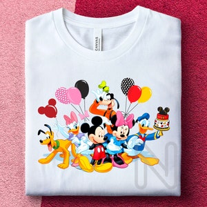 May include: White t-shirt with a colorful graphic of Mickey Mouse, Minnie Mouse, Donald Duck, Goofy, and Pluto celebrating with balloons and a birthday cake.