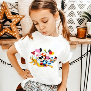 May include: A white t-shirt with a colorful graphic of Mickey Mouse and friends holding balloons. The graphic features Mickey Mouse, Minnie Mouse, Donald Duck, Goofy, Pluto, and other Disney characters.