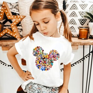 May include: A white t-shirt with a colorful Mickey Mouse silhouette made up of various Disney characters. The shirt has a ruffled neckline and short sleeves.