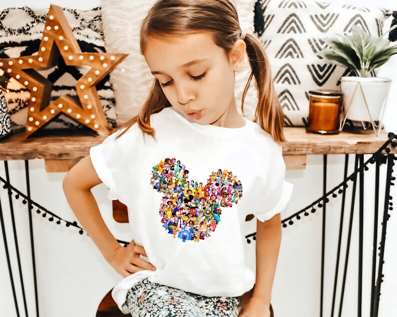 May include: A white t-shirt with a colorful Mickey Mouse silhouette made up of various Disney characters. The shirt has a ruffled neckline and short sleeves.