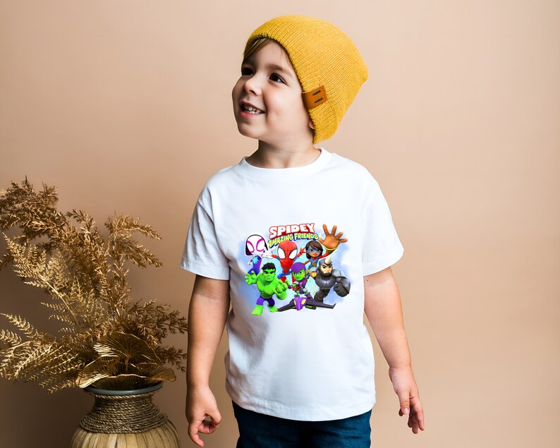 May include: A white t-shirt with a colorful graphic of Spider-Man and his friends. The graphic says "Spidey Amazing Friends".