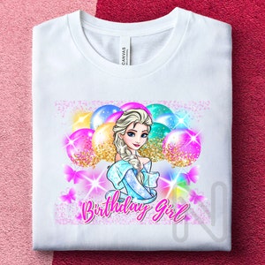 Puede incluir: Camiseta blanca con un gráfico de una niña con cabello rubio y ojos azules que lleva un vestido azul y sostiene globos. Los globos son rosas, amarillos y azules con brillo. El texto "Birthday Girl" está escrito en letras rosas.