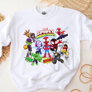 Peut inclure: Sweat-shirt blanc avec un imprim&eacute; graphique color&eacute; de Spider-Man et ses amis. L'impression comprend le texte "Marvel Spidey Amazing Friends" et met en sc&egrave;ne des personnages comme Green Goblin, Spider-Gwen et Doc Ock.