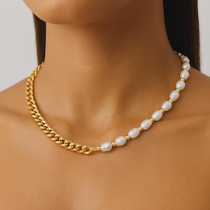 Può includere: Una collana dorata con una catena a maglia a un lato e una fila di perle bianche sull'altro. Le perle sono intervallate da piccole perline dorate, creando un design bicolore. La collana è indossata intorno al collo.