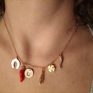May include: A gold chain necklace with multiple charms, including a horseshoe, a red chilli pepper, a four-leaf clover, a letter "U" charm, and a small hand charm.