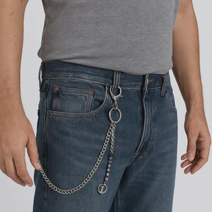 May include: Silver-toned chain wallet accessory attached to blue denim jeans. The chain features a lobster clasp, a key ring, and a decorative charm with the number 1. The chain is approximately 12 inches long.