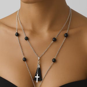 May include: Silver-toned necklace with black onyx beads and a black tassel pendant featuring a white cross. The necklace has a layered design with multiple strands and a large onyx bead at the bottom.