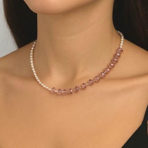 May include: A delicate necklace featuring a strand of small, white pearls that transitions into a series of faceted, pink-toned beads. The necklace is worn around the neck, showcasing the contrast between the two bead types.