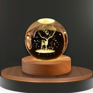 Könnte beinhalten: Eine Kristallkugel-Nachtlampe mit einem Hirsch-Design auf einem Holzsockel. Der Hirsch ist von Sternen umgeben und der Sockel ist aus Holz.