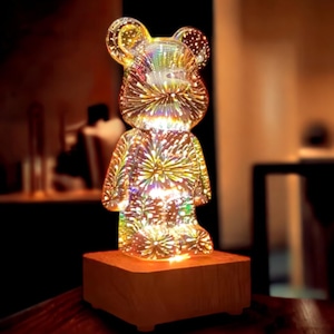Può includere: Una luce notturna a forma di orso in vetro con una finitura scintillante e iridescente. L'orso è in piedi su una base di legno.