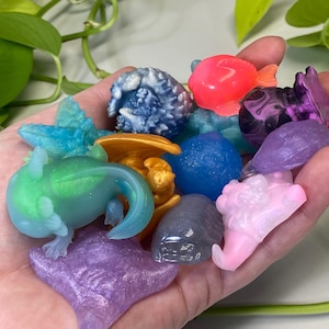 May include: A collection of small, colorful, resin figurines. The figurines are shaped like various creatures, including a dragon, a fish, and a turtle. The figurines are all hand-painted and have a glossy finish.