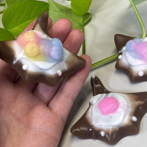 May include: Three brown and white star-shaped soaps with colorful swirls on top. The soaps are handmade and have a unique design.