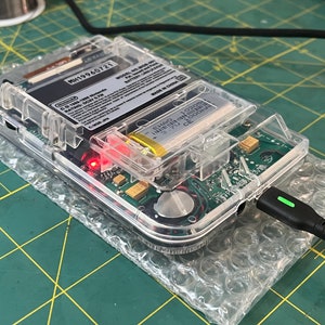 May include: A clear plastic case with a circuit board inside. The case has a battery and a charging port. The text on the circuit board reads "MH19960721 MODEL NO. 603-001 PATENT NO. 6,308,001 MADE IN CHINA".