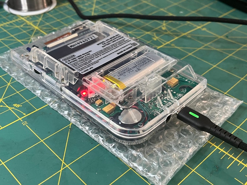 May include: A clear plastic case with a circuit board inside. The case has a battery and a charging port. The text on the circuit board reads "MH19960721 MODEL NO. 603-001 PATENT NO. 6,308,001 MADE IN CHINA".