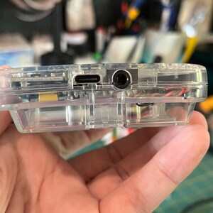May include: A clear plastic case with a USB-C port and a headphone jack on the side.
