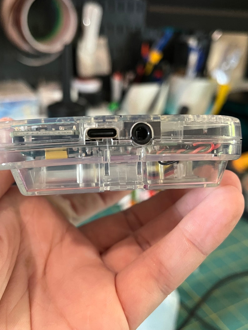 May include: A clear plastic case with a USB-C port and a headphone jack on the side.