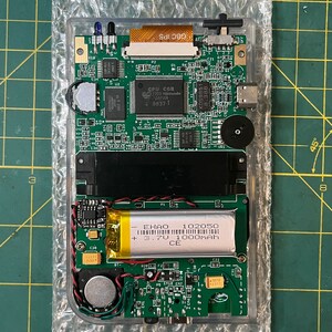 May include: Close-up of a green circuit board with a black and silver battery labeled "EHAO 102050 + 3.7V 1000mAh CE". The board has several components, including a small speaker, a switch, and a connector.
