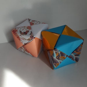 Pode incluir: Duas caixas de origami, uma com um padrão floral e papel cor de pêssego, a outra com um padrão azul e dourado.