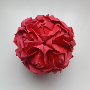 May include: A red origami rose, folded into a sphere shape. The rose is made of paper and has a delicate, intricate design.